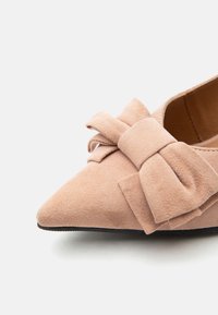 Μπεζ σουέντ επίπεδο παπούτσι με μυτερή μύτη, διακοσμημένο με μεγάλο φιόγκο στο πάνω μέρος και μαύρη λεία σόλα.