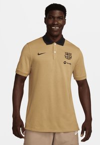 Tan poloshirt lavet af bomuld med en sort krave, udstyret med et Nike-logo og Barcelona-crest samt et Spotify-logo på venstre side.