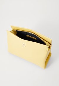 Clutch in pelle gialla con una texture liscia, chiusura con zip, foderatura interna nera e un logo inciso in modo discreto sul davanti.