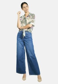 Floral short-sleeve shirt with a knot detail, paired with wide-leg blue denim jeans and beige high-heeled shoes.