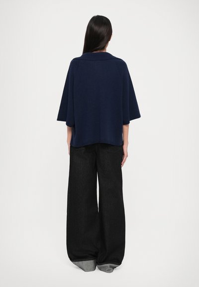Navy blue oversized villakangasta tehty paita, jossa on kaulus, yhdistettynä leveälahkeisiin mustiin denim-housuihin, joissa on kontrastivärinen cuff. Rentoa istuvuutta, minimaalista yksityiskohtaa.