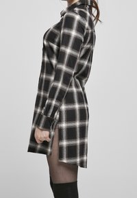 Abito a camicia a quadri bianco e nero con bottoni frontali, maniche lunghe, spacco laterale e una linea rilassata, realizzato in tessuto tessuto.