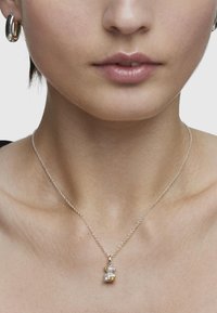 Collana in argento con pendente a forma di orso in perla e dettagli in oro. Il pendente presenta un design testurizzato e multicolore.