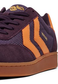 Lila Wildlederschuhe verfügen über orangefarbene synthetische Streifen und Details, mit einem strukturierten Mesh-Obermaterial und einer Gummisohle, die das sportliche Design betonen.