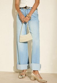 Jeans a gamba larga di colore azzurro chiaro con risvolti, canotta bianca a coste, scarpe con tacco blocco metalliche dorate e borsa in perle bianche dalla texture.
