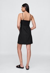 Čierne šaty s nastaviteľnými tenkými ramienkami, našitým zadným dielom a voľným strihom. Mäkká textúra a dizajn po kolená.