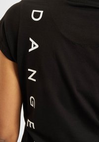Černé bavlněné tričko s krátkými rukávy, s velkým bílým textem "DANGER" vertikálně podél strany. Hladká textura, ležérní design.
