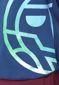 Tmavě modrá látka se velkým abstraktním grafickým vzorem v odstínech zelené a světle modré. Zaoblený lem a měkký, strukturovaný povrch.