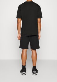 Svart kortärmad t-shirt i kombination med svarta träningsshorts, bärs med svarta sneakers med vitt varumärke. Enkel, avslappnad design.