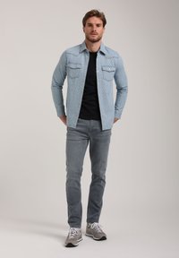 Lichtblauw gedessineerd denim overhemd met twee borstzakken, gecombineerd met een zwart t-shirt en grijze slim-fit jeans, afgewerkt met grijze sneakers.