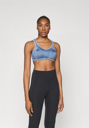 Top desportivo azul com padrão, com alças largas e decote redondo, combinado com leggings pretas de cintura alta. Textura de tecido suave.