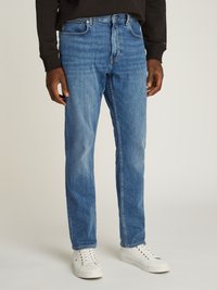 Vaqueros de mezclilla azul claro con corte recto, cinco bolsillos y un ligero desgaste. Combinados con zapatillas blancas, centrándose en la comodidad y la versatilidad.