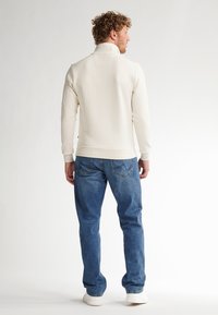 Pulover crem din fleece cu guler înalt, manșete și tiv nervurate; asortat cu blugi denim albaștri și adidași albi.