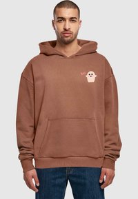 Felpa con cappuccio marrone, dotata di tasca frontale, polsini a costine e una grafica di un fantasma rosa con la scritta "Boo!" sul lato sinistro del petto.