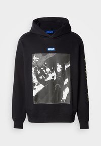 Μαύρο φούτερ με κουκούλα που διαθέτει εκτύπωση γραφικών στο μπροστινό μέρος, με λεπτομέρειες σε αντίθετες λευκές και γκρι αποχρώσεις. Λογότυπο και κείμενα σε μπλε και χρυσό χρώμα.