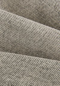 Katoenen denim stof in een lichtbeige tint, met een fijne diagonale weefstructuur en subtiele donkere spikkels. Glad oppervlak met een lichte glans.