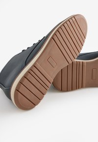 Navy blue leather sneakers with a rounded toe, cream midsole, and brown rubber outsole featuring horizontal grooves for traction.