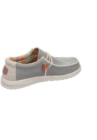 Zapato deslizante de tela gris con suela beige contrastante, cordones decorativos y forro interior vibrante y estampado. Presenta un diseño casual y punta redondeada.