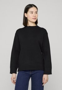 Pull noir en tricot avec un col rond, des poignets et un ourlet côtelés, et une coupe décontractée. Associé à un jean bleu.