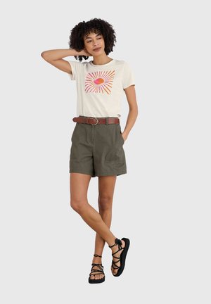 T-shirt crema con una grafica di sole colorata, abbinata a pantaloni corti verde oliva e una cintura marrone, completata da sandali neri con listini.