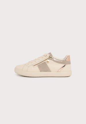Beige sneaker med guldfarvet lynlås, lyserøde metalliske detaljer, ruskindssidepatch, flade snørebånd og gummisål på ensfarvet hvid baggrund.