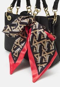 Sac en cuir texturé noir avec quincaillerie dorée, présentant une écharpe à motifs en noir et or avec des accents rouges nouée autour de la poignée.