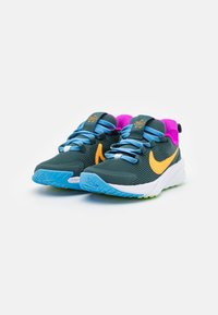 Tenisky v tmavozelenej farbe s ribbed textúrou, s modrými šnúrkami, ružovými akcentmi a oranžovým logom Swoosh. Biela a zelená gumová podrážka.