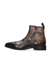 Botas de tobillo de cuero marrón con un acabado suave, punta afilada, dos hebillas plateadas y un diseño texturizado. Suela de goma negra sólida.