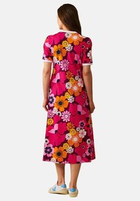 Kukkakuosi mekko vaaleanpunaisena, oranssina ja valkoisena. Lyhyet hihat valkoisilla resoreilla, polvipituinen, valmistettu kevyestä kankaasta. Yhdistettynä vaaleisiin kenkiin.