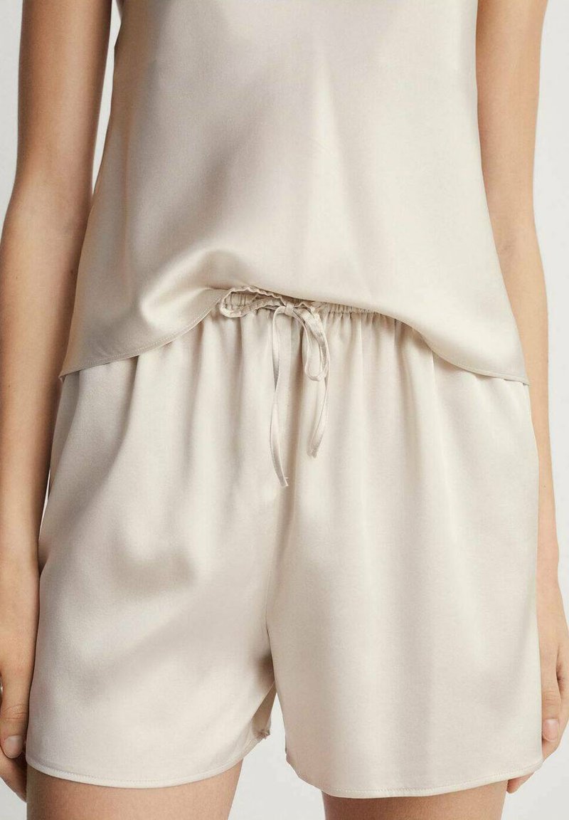 Tirantes de seda beige con un corte holgado, combinados con pantalones cortos a juego con una cinturilla elástica y cordón para mayor comodidad ajustable.