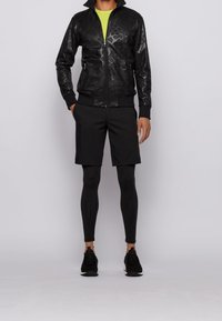 Black leather jacket with textured patterns, paired with black shorts and fitted leggings. Lime green undershirt and black athletic shoes.