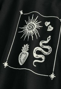 Čierna látka zdobená bielymi ilustráciami: slnko, had, ananás v tvare srdca a dve srdcia, rámované dekoratívnymi okrajmi.