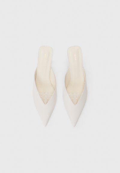 Beige spetsiga mules med en V-formad utskärning fram, med en texturerad spetsaccent på sidorna och en slät innersula.