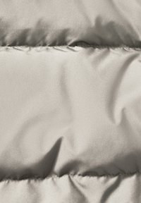 Giacca puffer grigia chiara in tessuto con una trama liscia e lucida, caratterizzata da sezioni trapuntate. Le linee di cucitura visibili creano motivi orizzontali.