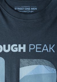 Mörkgrå bomulls-T-shirt med rund hals och tryckt text "ROUGH PEAK" i ljusblått samt mönstrade detaljer längst ner till höger.