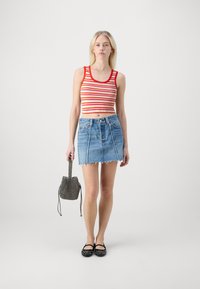 Top court rayé rouge et jaune, mini jupe en denim à ourlet effiloché, ballerines noires à clous, et un sac seau noir texturé.