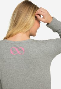 Grå sweatshirt med lång ärm, prydd med en rosa oändlighetssymbol på baksidan. Materialet verkar mjukt med en avslappnad passform och lätt textur.