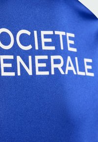 Blå textilbakgrund med vit text som lyder "SOCIETE GENERALE." Tyget har en mjuk textur och lätt glans som framhäver tydligheten i bokstäverna.
