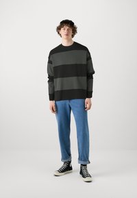 Mustvalge ja halliriba sweatshirt pikkade varrukatega, koos helesiniste lõdveste teksade ja mustade kõrgete tossudega.
