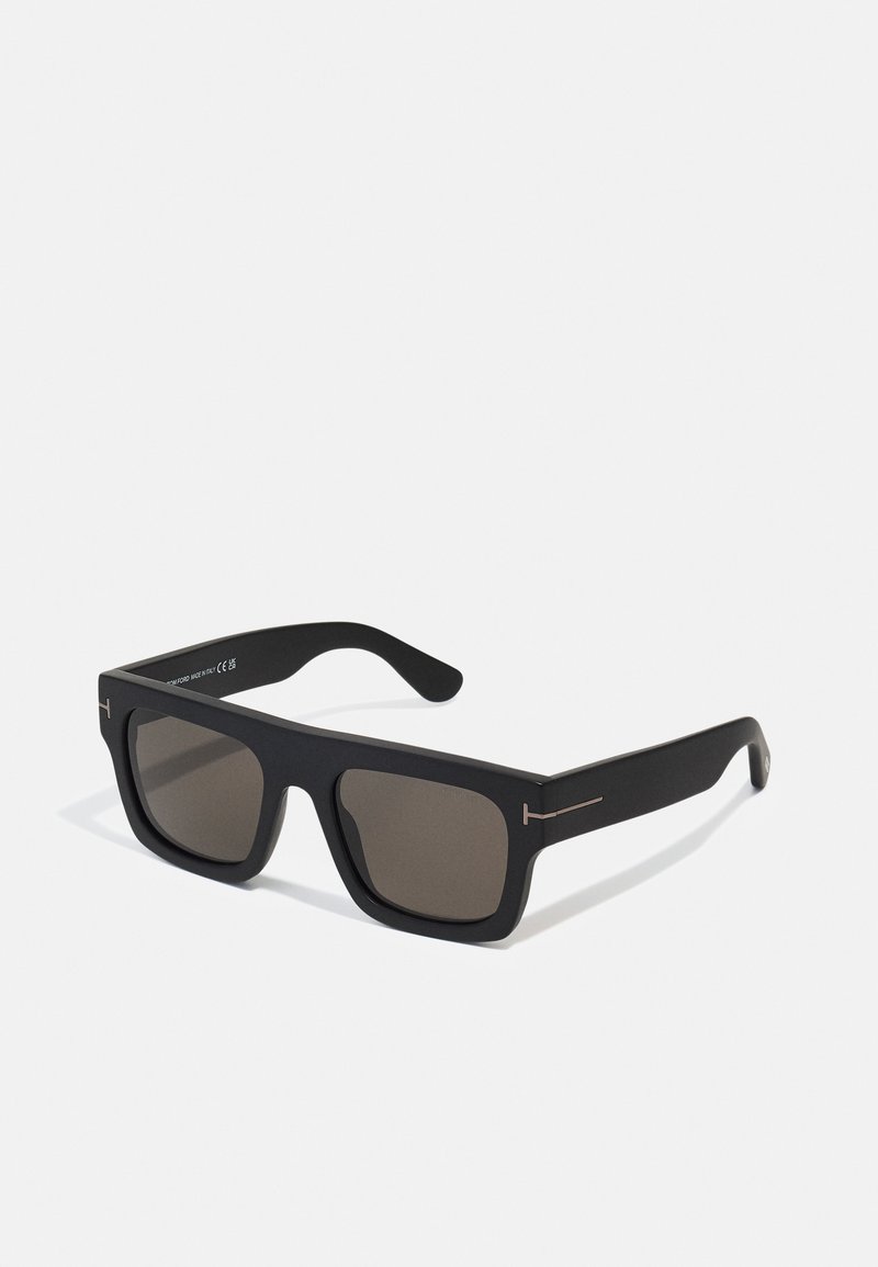 Lunettes de soleil rectangulaires noires avec des verres sombres. Fini mat, avec des accents métalliques subtils sur les branches. Aucune logo de marque visible.