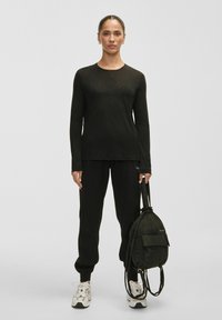 Long-sleeve black top, black sweatpants, and a black fabric backpack. Light, textured material; relaxed fit; neutral footwear with accents.