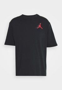T-shirt en coton noir à manches courtes, avec un logo Jumpman rouge sur le côté supérieur gauche de la poitrine, coupe décontractée et col ras du cou.