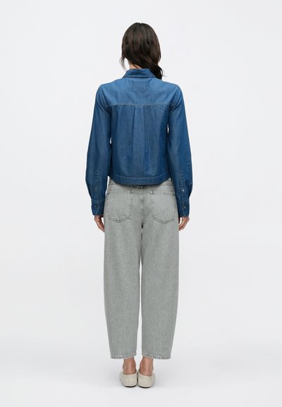 Veste en jean bleu foncé, à coupe droite, manches longues et détails à boutons, associée à un jean taille haute gris clair à jambes larges.