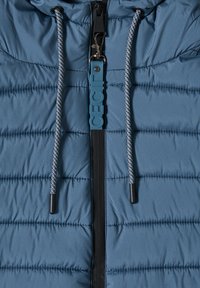 Pufferjack in donkerblauw, met horizontale stiksels, een zwarte ritssluiting en een blauwe merkritstag. De trekkoorden hebben reflecterende accenten.