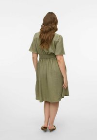Grøn, kortærmet kjole med indsnøret talje, flydende skirt og struktureret stof. Design med skulder- og midt-ryg længde.