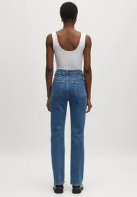 Jeans de mezclilla azul de tiro alto con un ajuste relajado y bolsillos traseros, combinados con una camiseta sin mangas blanca. Textura suave y piernas rectas.