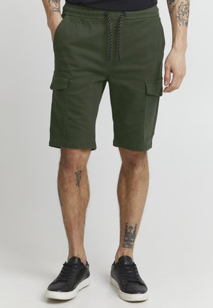Cargo-Shorts in dunklem Grün, elastischer Bund mit Kordelzug, multiple Taschen, strapazierfähiger Stoff, schlichtes Design, getragen mit schwarzen Sneakers.