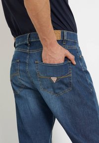 Jeans in denim blu scuro con una finitura testurizzata. Presentano un'etichetta con il logo sulla vita e una cucitura distintiva sulle tasche.