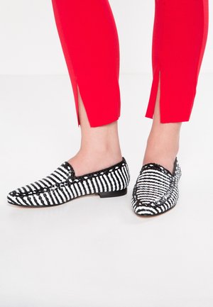 Mocasines de rayas en blanco y negro hechos de tela con un tacón bajo. Los zapatos presentan un diseño trenzado y una textura flexible y suave.