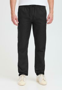 Black trousers with an elastic waistband and drawstring, featuring a straight cut and smooth cotton fabric. Paired with white sneakers.